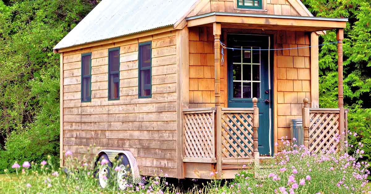 Ein Tiny House aus Holz steht auf einer Wiese.
